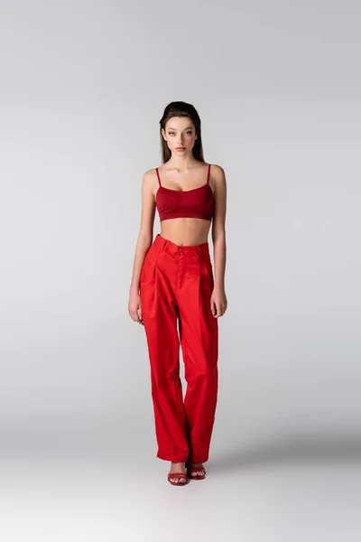 Longitud completa del modelo en top rojo y pantalones posando sobre gris - foto de stock