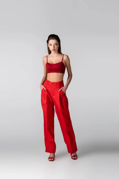 Full length of model in crop top and red pants posing with hands in pockets on grey — Stock Photo