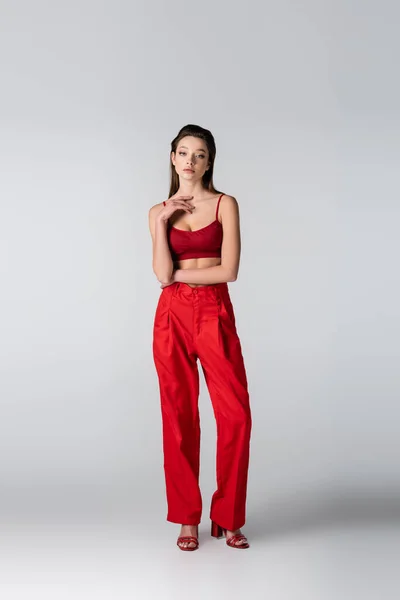 Tutta la lunghezza del modello in crop top rosso e pantaloni in piedi sul grigio — Foto stock