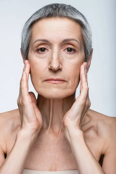 Middle aged woman touching face with wrinkles isolated on grey — Stock Photo