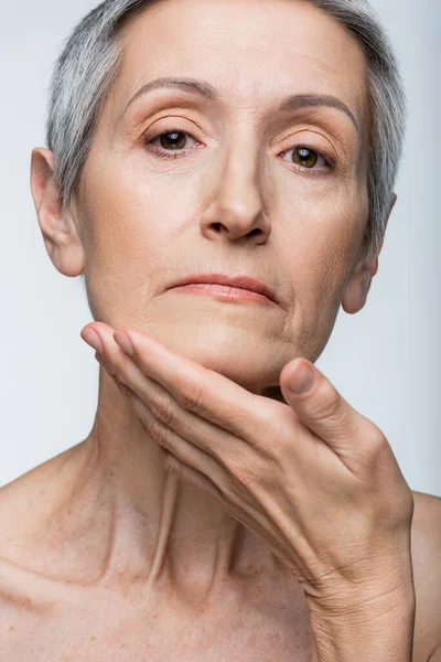 Mujer de mediana edad tocando la barbilla aislada en gris - foto de stock