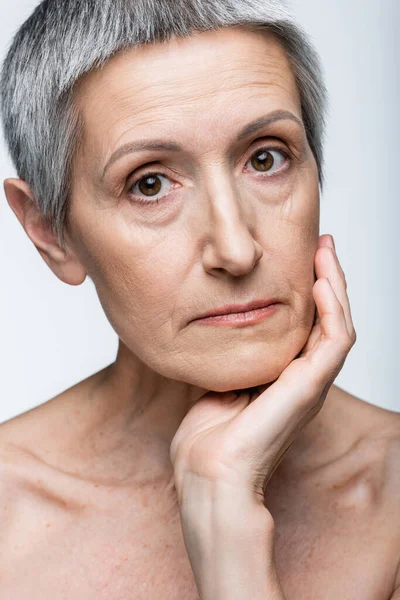 Mujer de mediana edad tocando mejilla aislada en gris - foto de stock