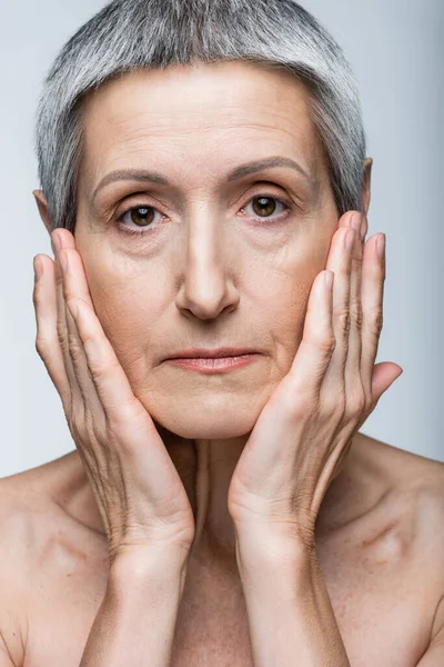 Middle aged woman touching cheeks isolated on grey — Stock Photo