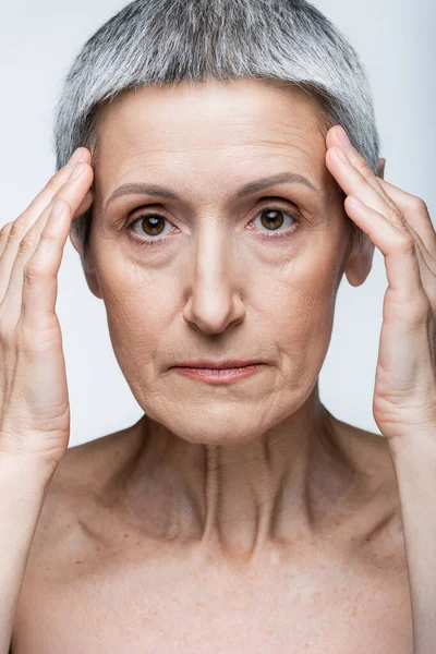 Middle aged woman with wrinkles touching temples isolated on grey — Stock Photo