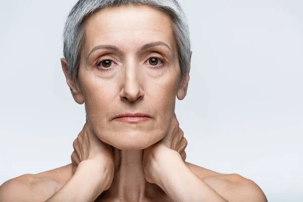 Donna di mezza età toccando il collo isolato sul grigio — Foto stock