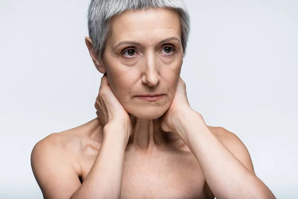 Mujer madura con hombros desnudos tocando el cuello aislado en gris — Stock Photo