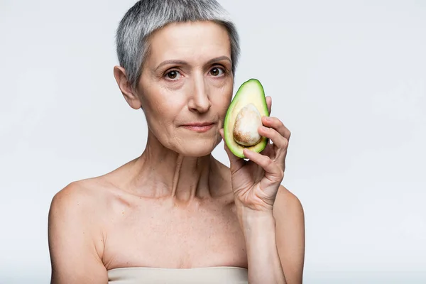 Middle aged woman holding half of avocado isolated on grey — Stock Photo