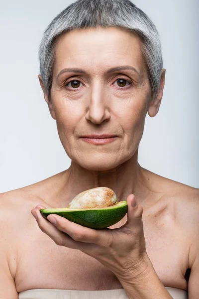 Женщина средних лет с половиной спелого авокадо, изолированного на сером — стоковое фото