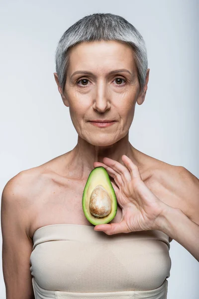 Femme d'âge moyen tenant la moitié de vert et avocat mûr isolé sur gris — Photo de stock