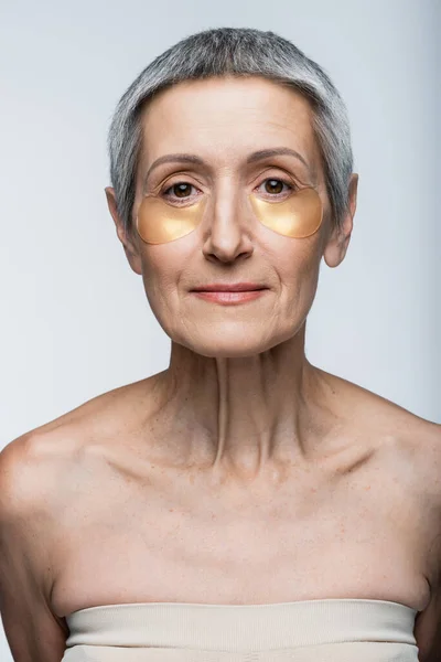 Женщина средних лет в глазных повязках, смотрящая на камеру, изолированную на сером — стоковое фото