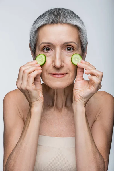 Donna di mezza età con cetrioli tagliati verdi isolati su grigio — Foto stock