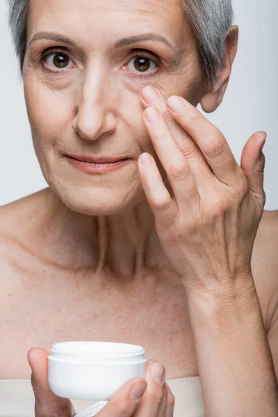 Mature woman applying anti-wrinkle cream isolated on grey — Stock Photo