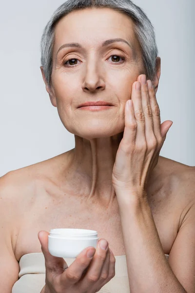 Mujer de mediana edad aplicando crema antiarrugas aislada en gris - foto de stock