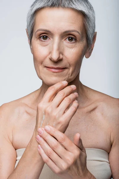 Middle aged woman applying cream on hand isolated on grey — Stock Photo