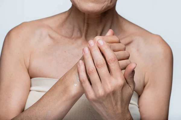 Vue partielle de la femme d'âge moyen appliquant de la crème sur la main isolée sur gris — Photo de stock