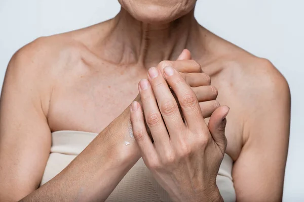 Partial view of middle aged woman applying cream on hand isolated on grey — Stock Photo