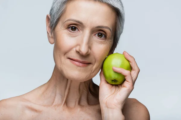 Alegre mujer de mediana edad sosteniendo manzana verde aislado en gris - foto de stock