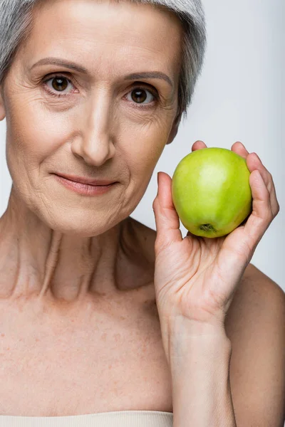 Middle aged woman holding ripe apple isolated on grey — Stock Photo