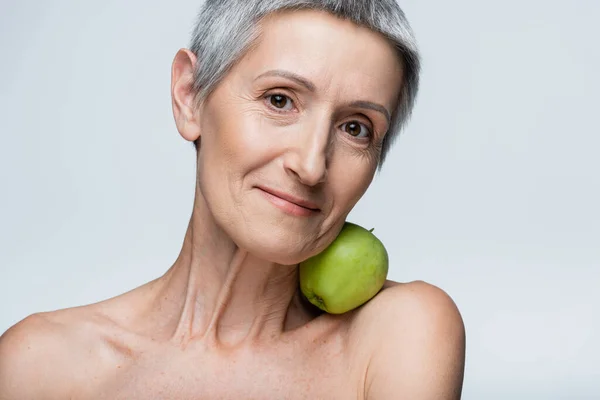 Smiling mature woman holding green apple with neck isolated on grey — Stock Photo