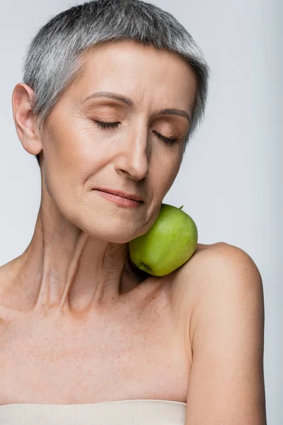 Femme mûre souriante aux yeux fermés tenant la pomme verte isolée sur gris — Photo de stock