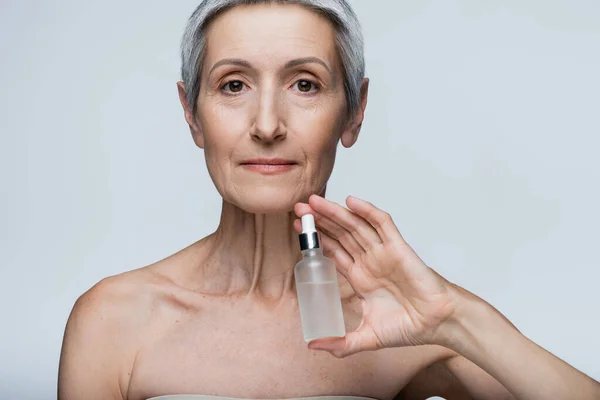 Middle aged woman holding bottle with serum isolated on grey — Stock Photo