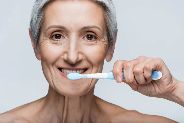 Felice donna di mezza età in possesso di spazzolino da denti e lavarsi i denti isolati su grigio — Foto stock