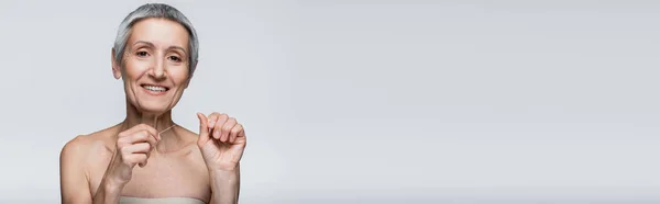 Happy middle aged woman with grey hair holding dental floss isolated on grey, banner — Stock Photo