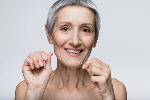 Positive middle aged woman with grey hair holding dental floss isolated on grey — Stock Photo