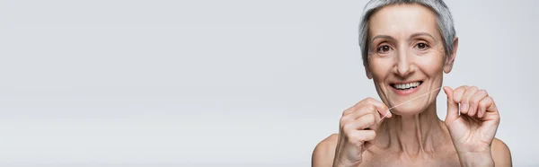 Femme d'âge moyen positive avec des cheveux gris tenant fil dentaire isolé sur gris, bannière — Photo de stock
