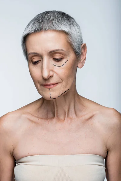 Femme mature aux épaules nues et aux lignes marquées sur le visage regardant vers le bas isolé sur le gris — Photo de stock