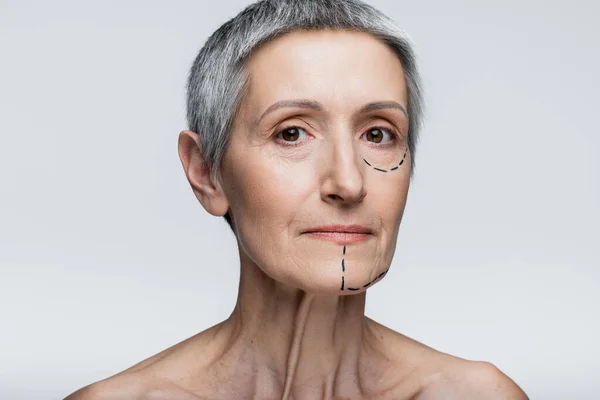 Mature woman with marked lines on face looking at camera isolated on grey — Stock Photo