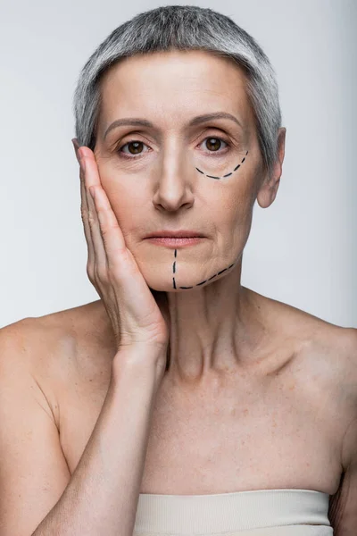 Mature woman with wrinkles and marked lines looking at camera isolated on grey — Stock Photo