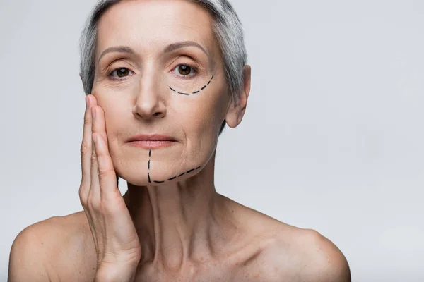 Mature woman with wrinkles and marked lines touching face isolated on grey — Stock Photo