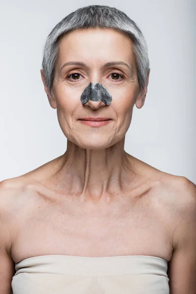 Улыбающаяся зрелая женщина с черным пятном на носу, изолированная от серого — стоковое фото
