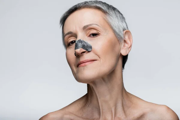 Cheerful and mature woman with black patch on nose isolated on grey — Stock Photo