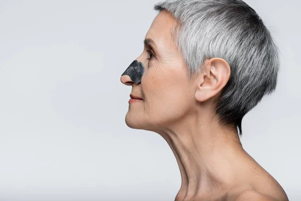 Side view of smiling and mature woman with black patch on nose isolated on grey — Stock Photo