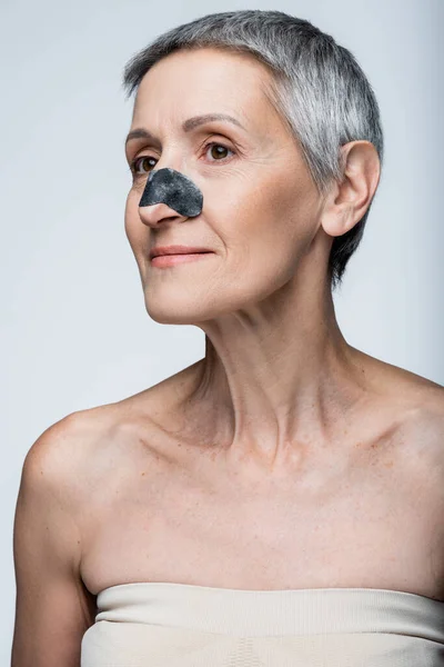 Pleased middle aged woman with black patch on nose isolated on grey — Stock Photo