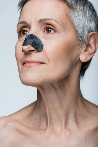 Donna matura sorridente con capelli grigi e patch nera sul naso isolato su grigio — Foto stock