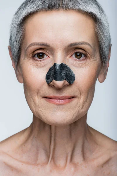 Primer plano de la sonriente mujer de mediana edad con el pelo gris y parche en la nariz aislado en gris - foto de stock