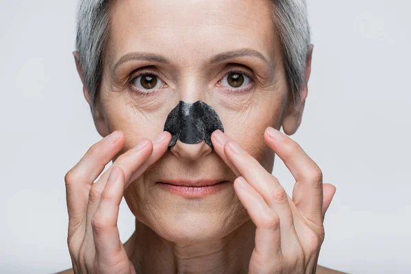 Close up of mature woman with grey hair and applying patch on nose isolated on grey — Stock Photo