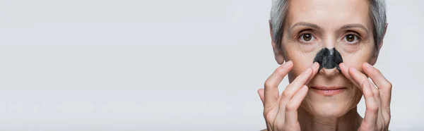 Primer plano de la mujer madura con el pelo gris y la aplicación de parche en la nariz aislado en gris, bandera - foto de stock