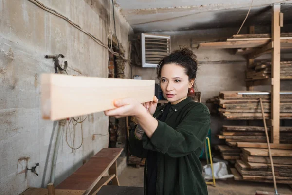 Young carpenter looking at wooden plank in workshop — Stock Photo