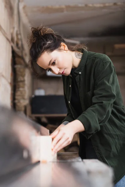 Татуированный дизайнер мебели держит размытую доску возле столярной машины — стоковое фото