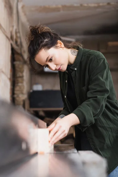 Designer de meubles tatoués tenant une planche floue près de la machine à menuisier — Photo de stock