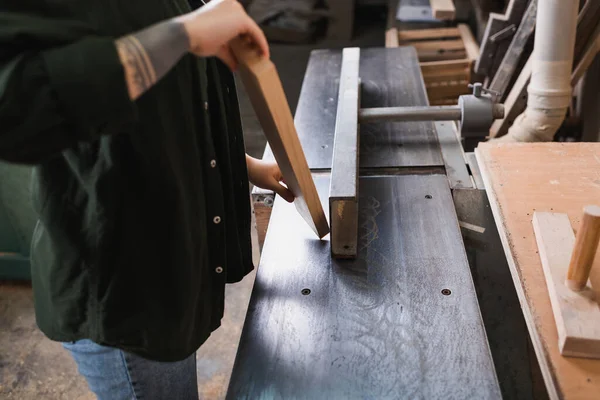 Обрезанный вид на татуированный плотник, держащий доску возле столярной машины в мастерской — стоковое фото
