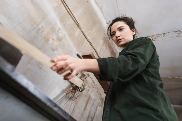 Niedrige Winkelaufnahme des Tischlers, der unscharfe Planke in der Nähe der Tischler-Maschine hält — Stockfoto