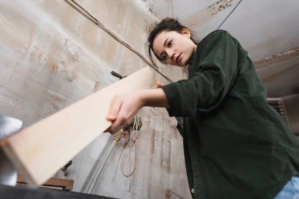 Low angle view of carpenter checking wooden plank in workshop — Stock Photo