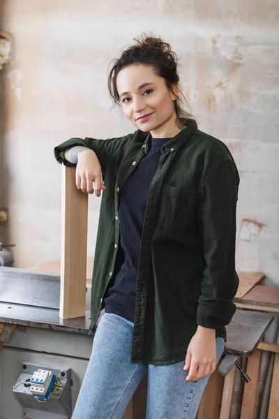 Lächelnder Tischler steht neben Holzplanke und Tischler-Maschine — Stockfoto