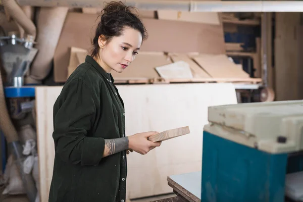 Junge Möbeldesignerin hält Planke nahe Dickenhobel in Werkstatt — Stockfoto