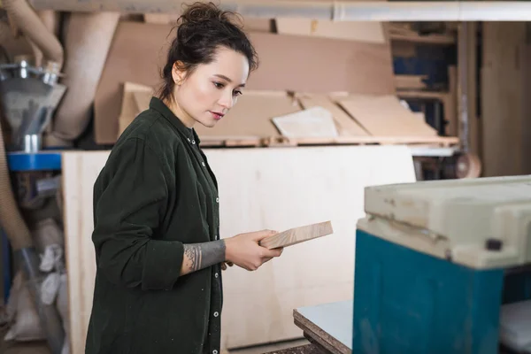 Jeune designer de meubles tenant planche près de raboteuse d'épaisseur dans l'atelier — Photo de stock